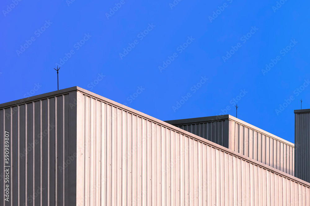 Aluminium Industrial Buildings with sunlight reflection on Corrugated Metal Wall surface against blue clear sky Background Aluminium Industrial Buildings with sunlight reflection on Corrugated Metal Wall surface against blue clear sky Background