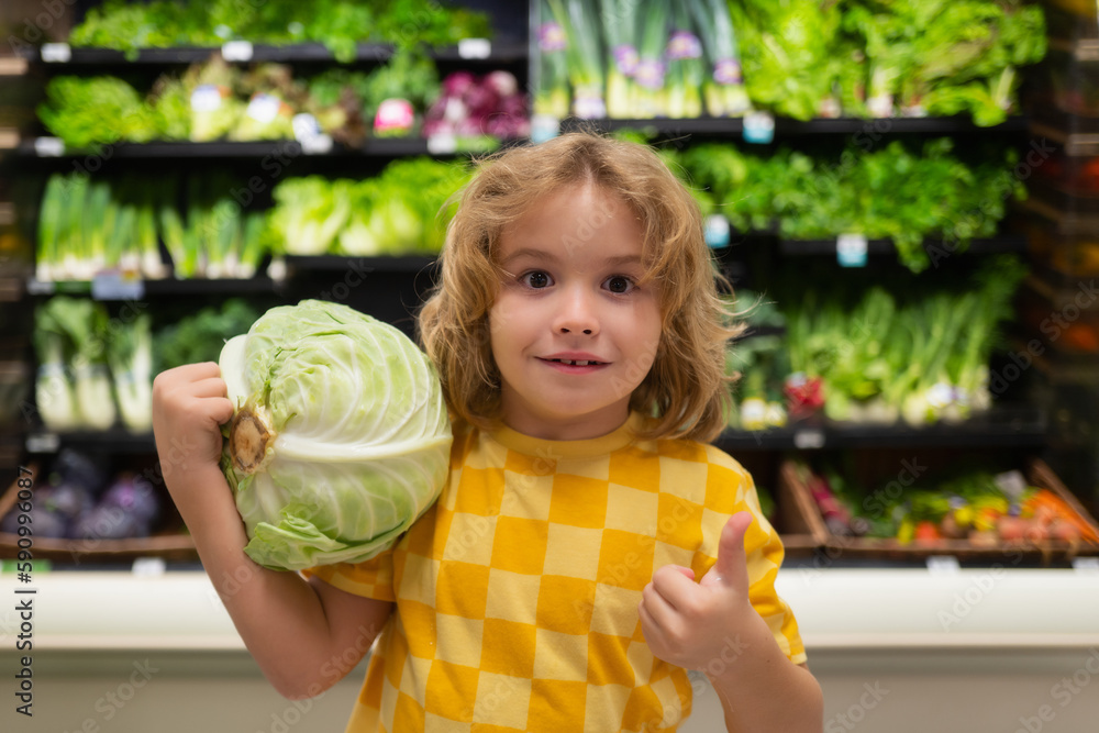 Fototapeta premium Child with cabbage. Child choosing fruits and vegetables during shopping at vegetable supermarket.