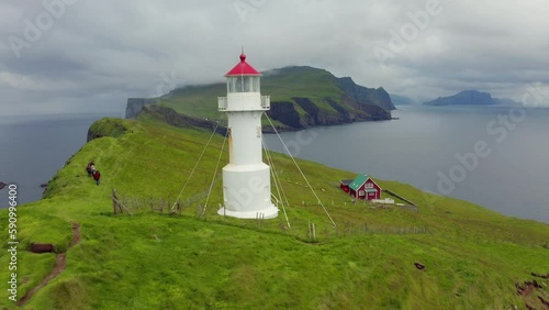 4k drone forward video (Ultra High Definition) of Mykines island with tourists and old lighthouse. Colorful morning view of Faroe Islands Denmark, Europe. Dramatic seascape of Atlantic ocean.