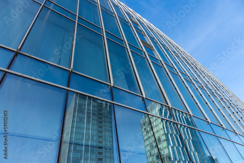 The blue sky is reflected in the windows of a modern office building. Architecture and exterior of contemporary houses