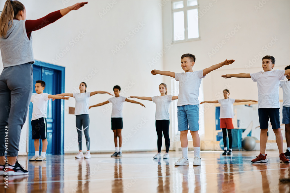 Naklejka premium Happy kids and their coach exercising during PE class at school.