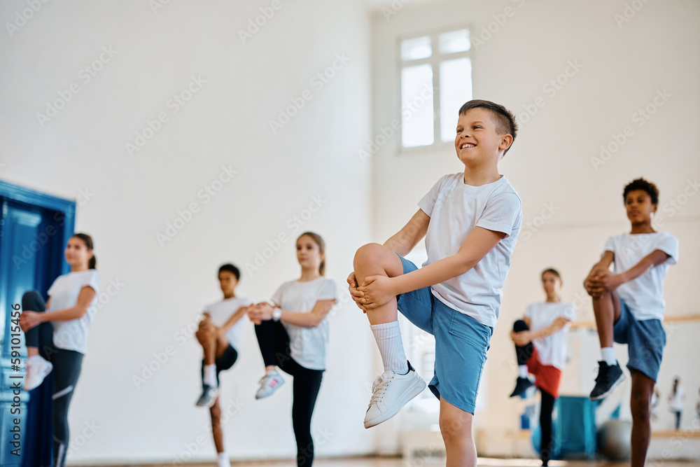 Happy schoolboy stretching his leg while having physical education class with his classmates.