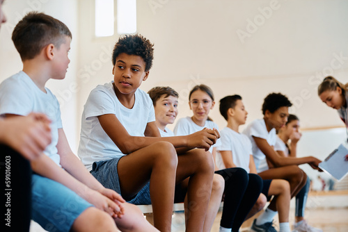 Multiracial group of elementary students talk during physical education class at school.