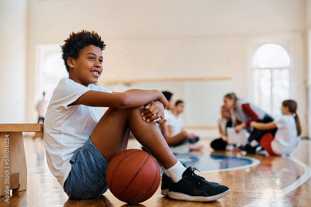 Naklejka premium Happy African American student relaxing on floor during PE class at school.
