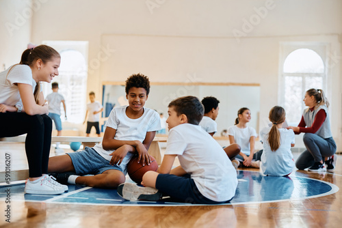 Happy black boy talks to his friends during physical activity class at school gym.