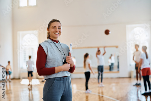 Fototapeta Naklejka Na Ścianę i Meble -  Young happy female coach during PE class at elementary school gym looking at camera.