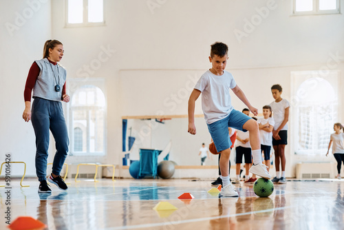 Fototapet Elementary student practicing with soccer ball during physical education class at school gym