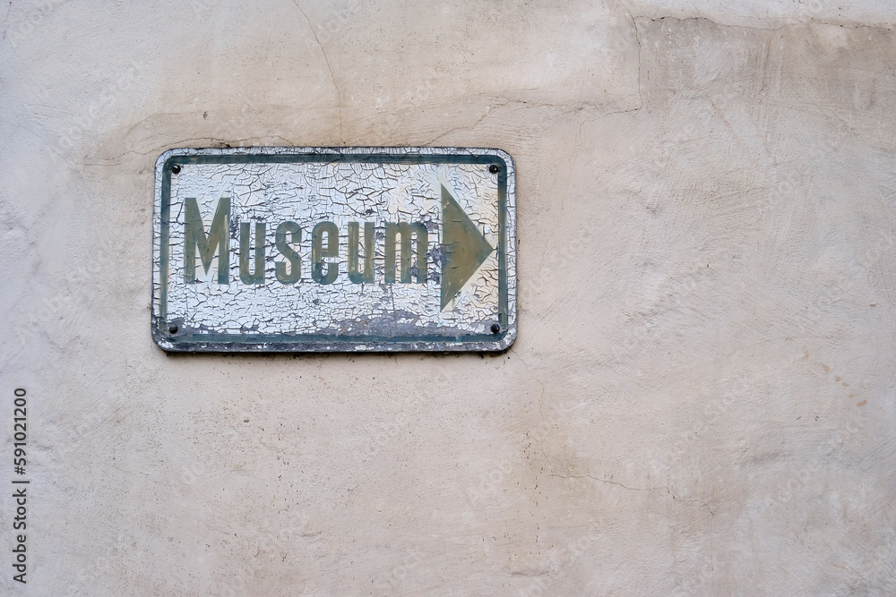 Yellowed and weathered sign full of cracked paint with a directional label saying MUSEUM painted on it. Yellowed and weathered sign full of cracked paint with a directional label saying MUSEUM painted on it.