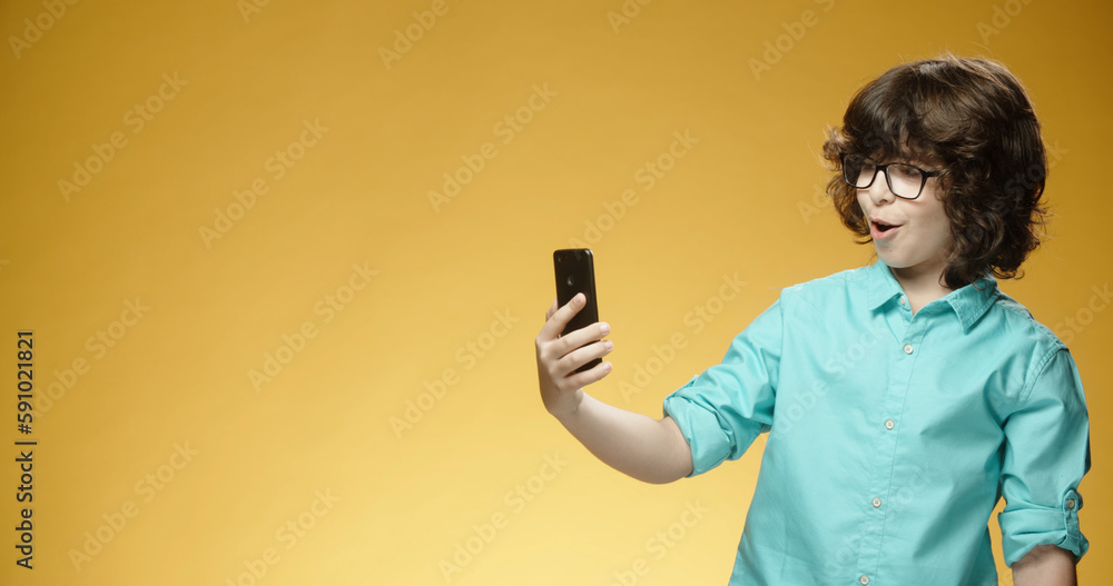 Little cheerful boy using his smartphone when suddenly getting surprised , isolated on yellow background - emotions concept close up Little cheerful boy using his smartphone when suddenly getting surprised , isolated on yellow background - emotions concept close up