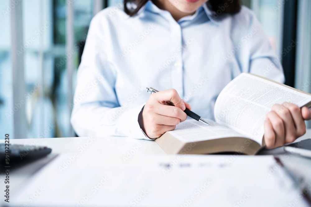 Portrait of Asian Business woman working from office taking reading and writing notes in note pad working on laptop computer in her workstation Portrait of Asian Business woman working from office taking reading and writing notes in note pad working on laptop computer in her workstation