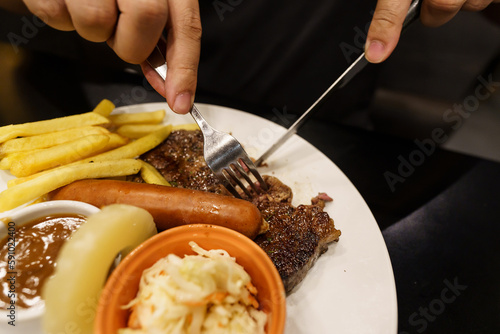 Man eating Grilled Meats stake from plate. hand holding knife and fork cutting grilled beef steak