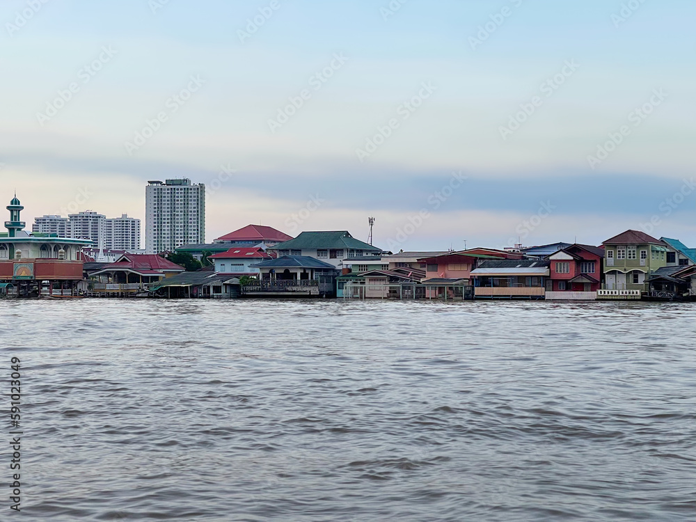 Houses stilts along Chao Phraya River. Bangkok city. Metropolis of SouthEast Asia, the capital of Thailand. Architecture on the river bank. View from the water. Krung Thep Maha Nakhon กรุงเทพมหานคร