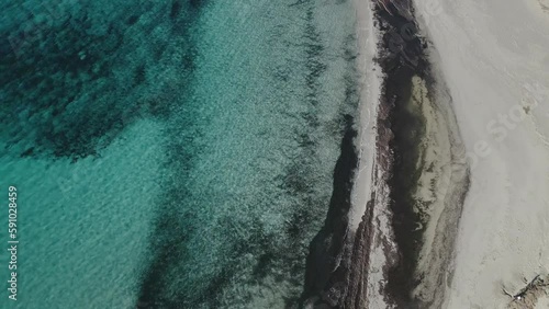 Slow cinematic drone flight over beach with white sand along the coastline of Menorca as waves wash ashore. photo