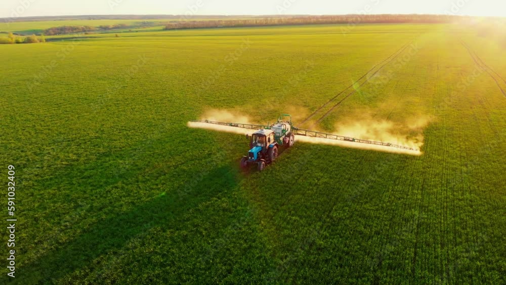 Aerial video of tractor spraying soil and young crop in springtime in field. Tractor spraying pesticides on soy field with sprayer at spring. Nozzle of the tractor sprinklers sprayed.