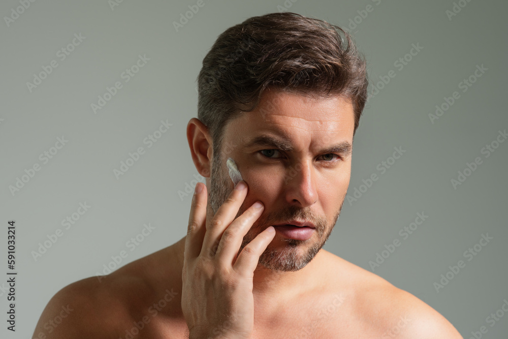 Fototapeta premium Man care of skin. Charming man with perfect soft skin. Male beauty and skincare concept. Man cosmetic, skin treatment. Morning hygiene. Mens cosmetics and wellness. Skincare. Man with cream on face.