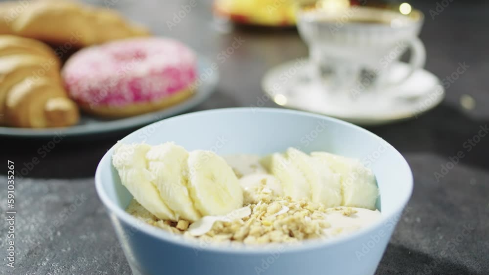 Close-up of a plate with muesli and yogurt on which a hand lays a banana. Healthy healthy breakfast for the whole family. Close-up of a plate with muesli and yogurt on which a hand lays a banana. Healthy healthy breakfast for the whole family.
