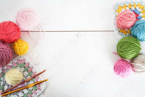 multicolored woolen balls with granny sqaure and crochet hook on white wooden ground with space for text photo