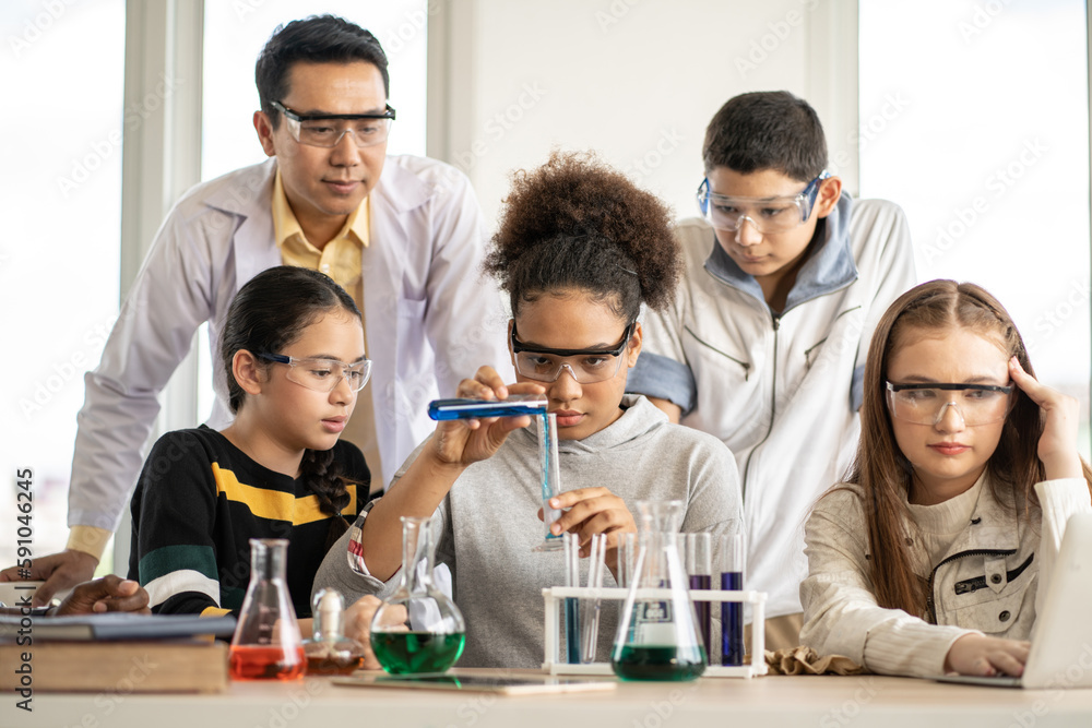 Fototapeta premium Diversity group of students in protective eyeglasses in science class doing chemical experiment in laboratory. Teacher watching girl mixing chemistry in test tube. learning and education concept