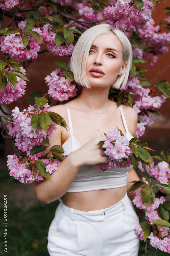 Sexy woman with short white hair in the sunlight on a beige background and a branch of blooming sakura. Sexy woman with short white hair in the sunlight on a beige background and a branch of blooming sakura.