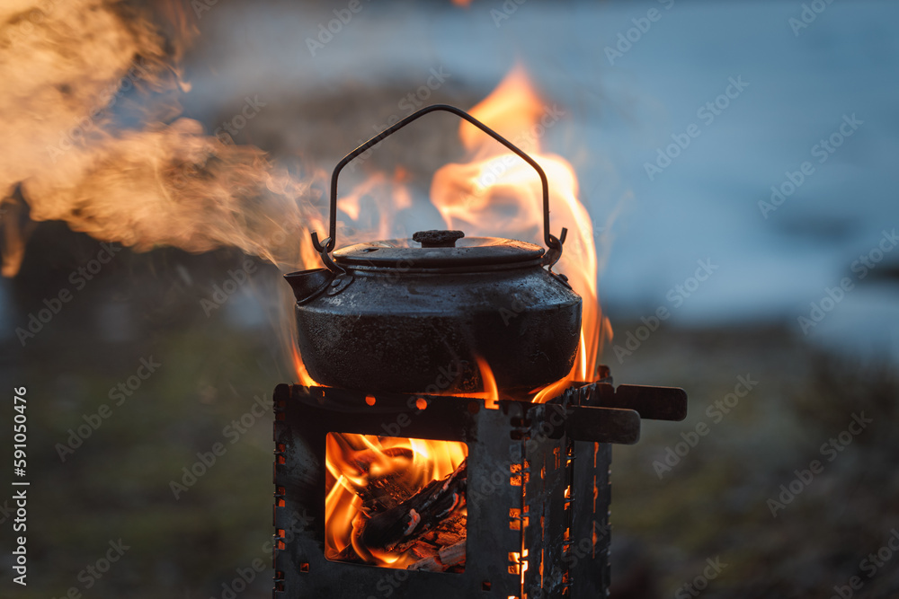 Kettle on a woodburning stove on a spring evening in the forest. Kettle in focus, background is