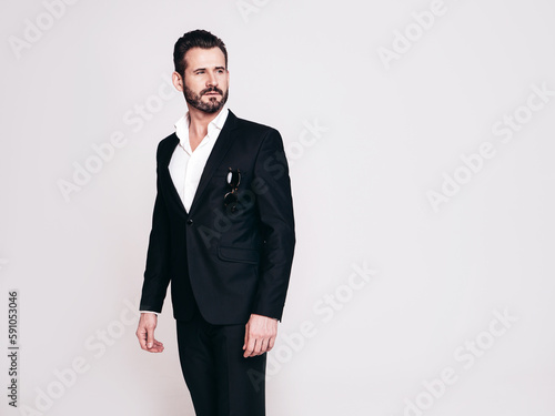 Portrait of handsome confident stylish hipster lambersexual model. Sexy modern man dressed in black elegant suit. Fashion male posing in studio, isolated on white. Holding sunglasses
