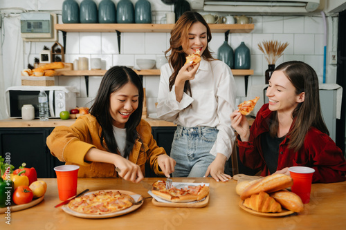 Group of friends making fun at home party.They sitting on desk in living room and eating pizza. happy