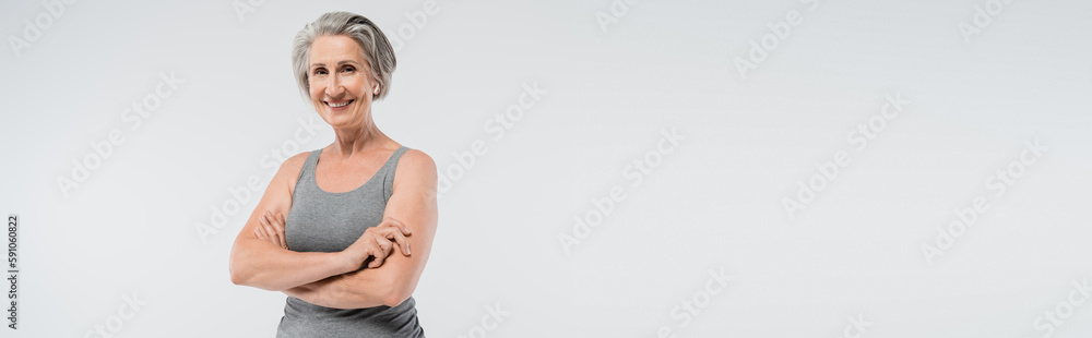 carefree senior woman in sportswear standing with folded arms isolated on grey, banner. carefree senior woman in sportswear standing with folded arms isolated on grey, banner.