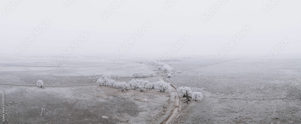 Aerial panoramic view of a snow covered landscape with a narrow lake on it on a foggy day