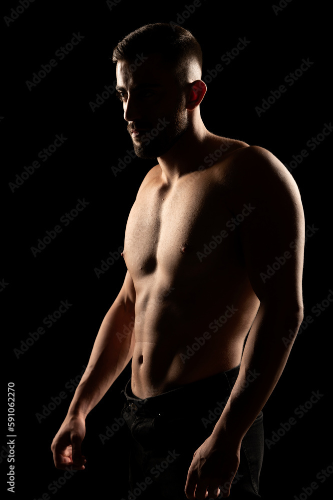 Silhouette of a muscular shirtless man in the shadow on a black background