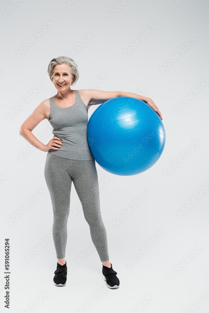 full length of happy senior woman in sportswear holding fitness ball on grey. full length of happy senior woman in sportswear holding fitness ball on grey.