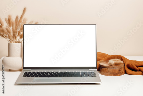 Laptop mockup on the table with ceramic vase, lagurus grass bouquet, wooden box and brown linen cloth with beige wall background. Laptop template for study, home office, website promotion, branding