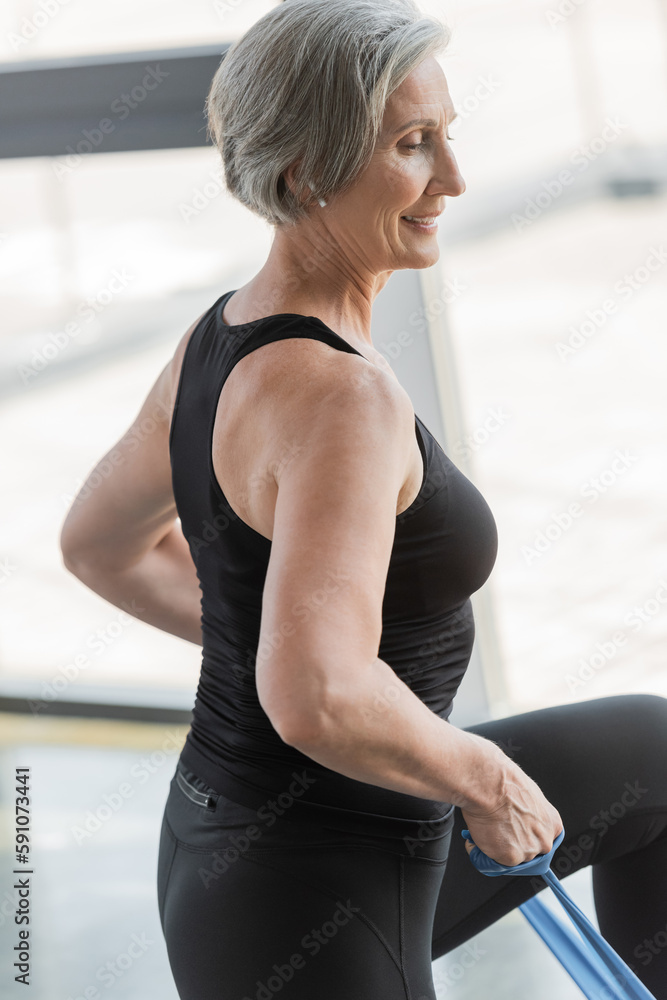 overjoyed senior woman in black leggings and tank top exercising with elastics.