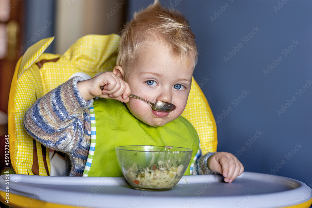 A little boy eats with a spoon by himself. A little boy eats with a spoon by himself.