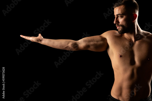 Torso of a young athletic guy with outstretched hand. concept: the male body after exercise and diet. men's health: shaved breasts on a dark studio background