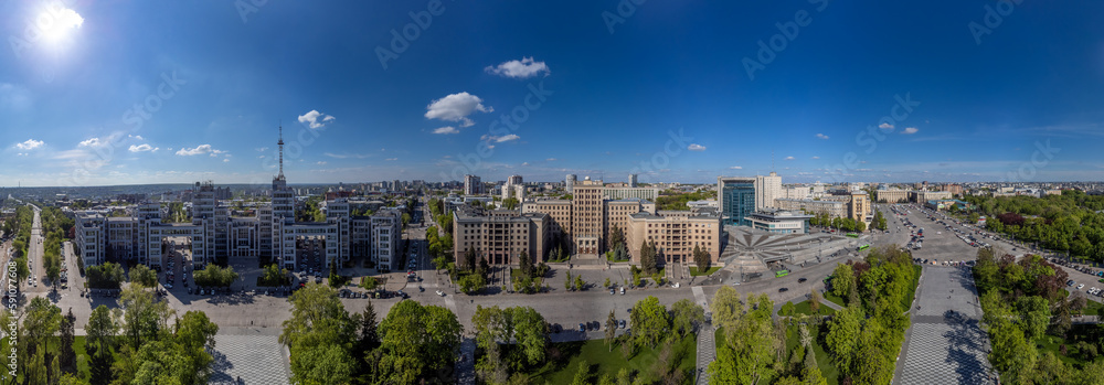 Aerial panoramic view on Derzhprom and northern Karazin National University buildings on Freedom Square with spring greenery and blue sky in Kharkiv, Ukraine