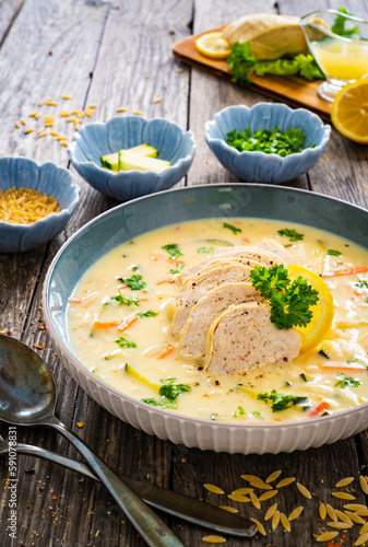 Greek lemon creamy soup with cooked chicken breast on wooden table