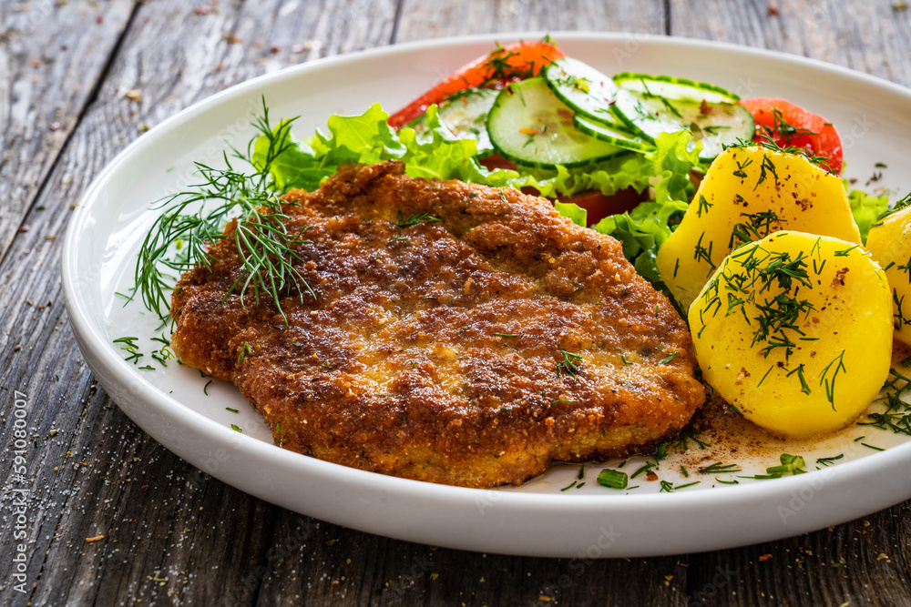 Breaded fried pork chop with fresh vegetable salad and potatoes on wooden table
Breaded fried pork chop with fresh vegetable salad and potatoes on wooden table