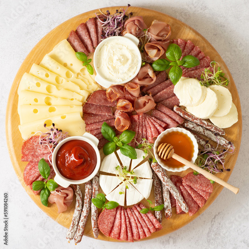 Sausage and cheese slicing on a round cutting board on a brown background.