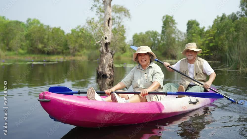 Asian senior couple kayaking together in the lake at mangrove forest on summer vacation. Retired elderly people man and woman have fun outdoor lifestyle travel nature and rowing a boat in the river. Asian senior couple kayaking together in the lake at mangrove forest on summer vacation. Retired elderly people man and woman have fun outdoor lifestyle travel nature and rowing a boat in the river.