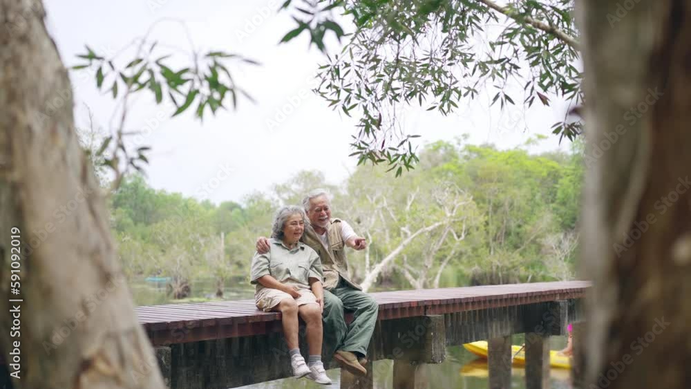 Happy Asian senior couple resting on wooden bridge and looking beautiful nature at tropical forest. Retired elderly people enjoy outdoor lifestyle travel nature hiking together on summer vacation. Happy Asian senior couple resting on wooden bridge and looking beautiful nature at tropical forest. Retired elderly people enjoy outdoor lifestyle travel nature hiking together on summer vacation.