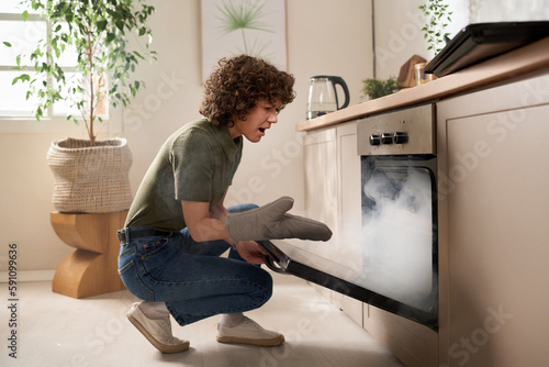 Housewife opening the oven door and taking out burnt food during her cooking in the kitchen photo