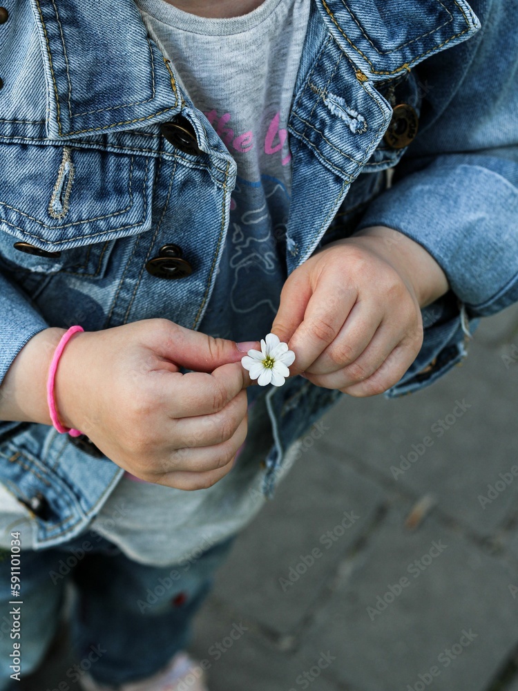 Vertical closeup shot of a little girl in a cute denim jacket holding flowers