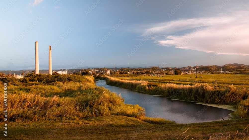 Obraz premium Scenic view of a narrow river flowing amid the fields under the blue sky