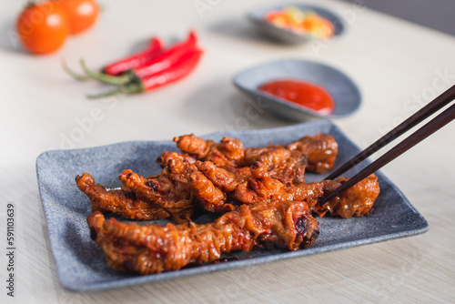 Spicy chicken feet or ceker ayam pedas with chili, tomato and sauce served with a plate on wooden white table photo