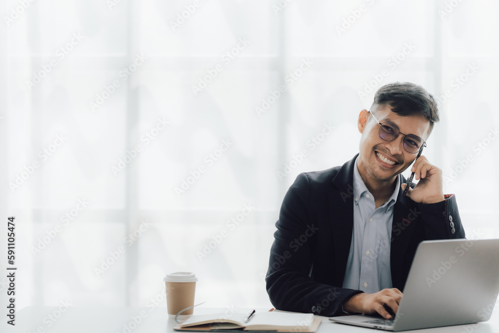 Happy working asian businessman talking on the phone with accounting documents at desk in happy working office
