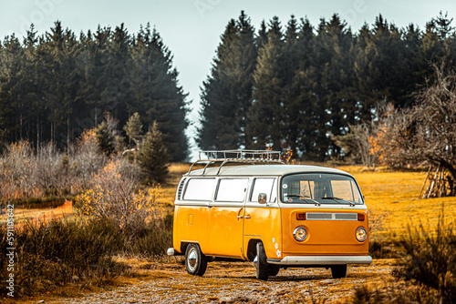 Volkswagen van t2 orange et blanc, garé dans un décor naturel en plein air