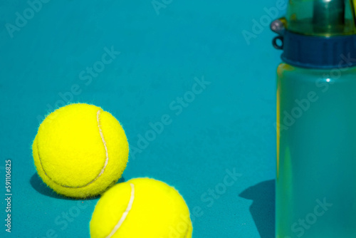 Tennis racket, ball and water bottle on hard blue court