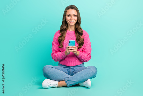 Full length photo of adorable stunning positive satisfied girl sitting floor use modern technology device isolated on cyan color background