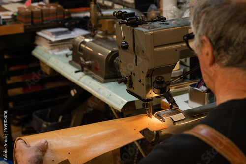 view of a leather craftsman   s shoulders sitting while sewing a leather back of a chair in his traditional workshop in the historic center of rome  italy