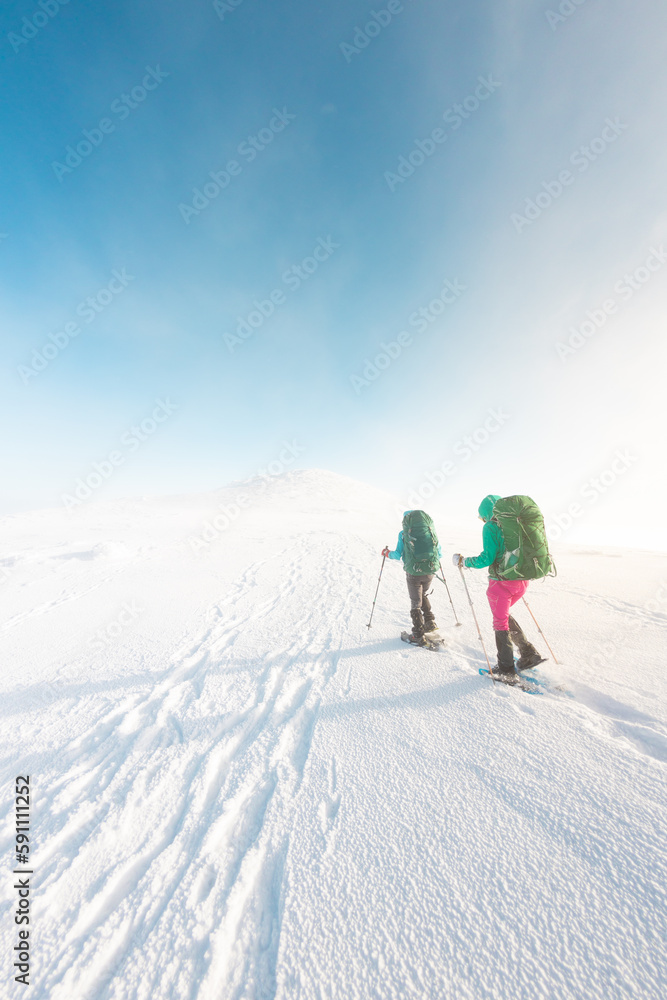 two girls in snowshoes walk in the snow. hiking in the mountains in winter.